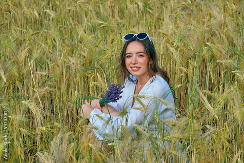 Portrait of a young girl in light clothes sitting in a wheat field