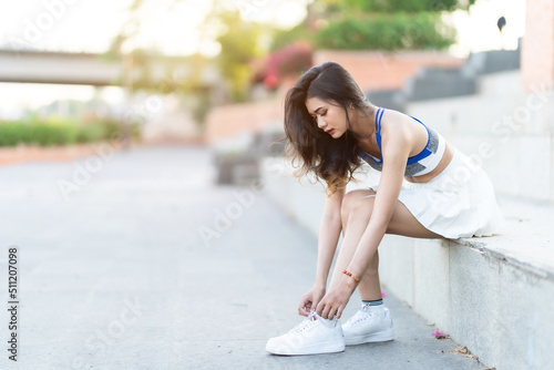 Portrait of beautiful athletic young asian woman in fashionable sportswear sit tie shoelaces and having rest after strong exercise training in garden the park,Outdoor Sporty concept