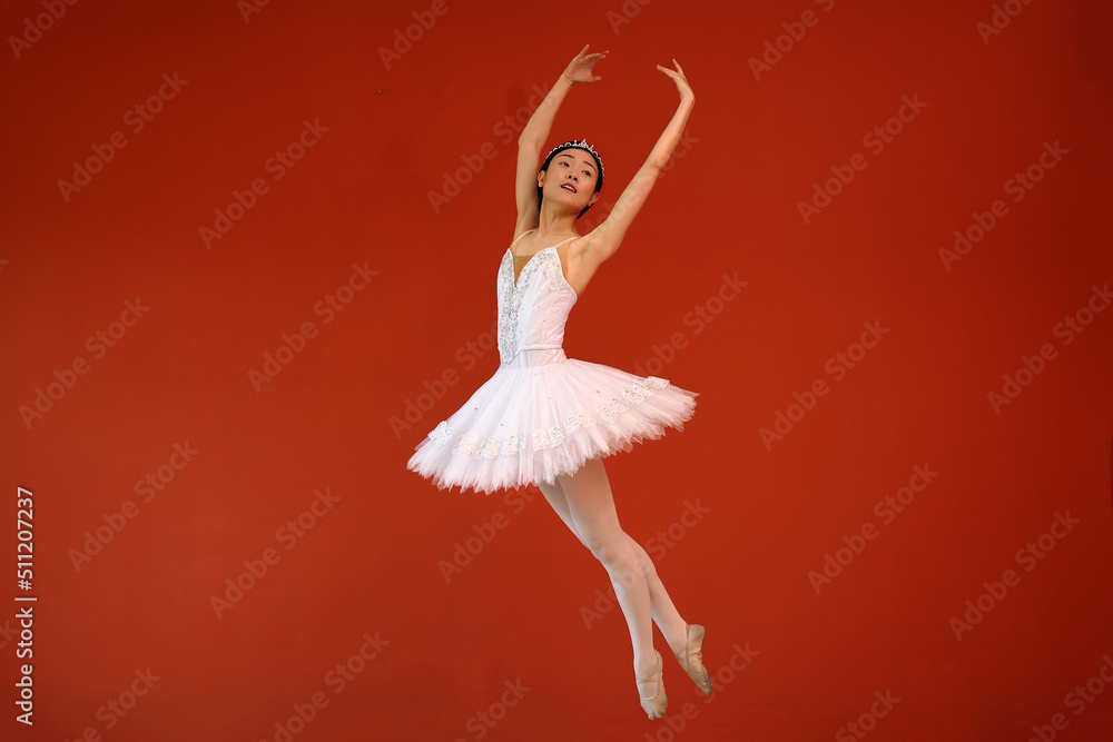 Fototapeta premium Beautiful Asian woman ballet dancer practice dance jump move wearing tutu at home red orange background wall