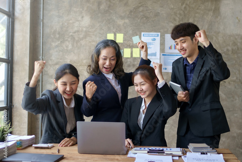Happy group of young Asian business people successful excited raised hands rejoicing with laptop computer in office. New startup project concept.