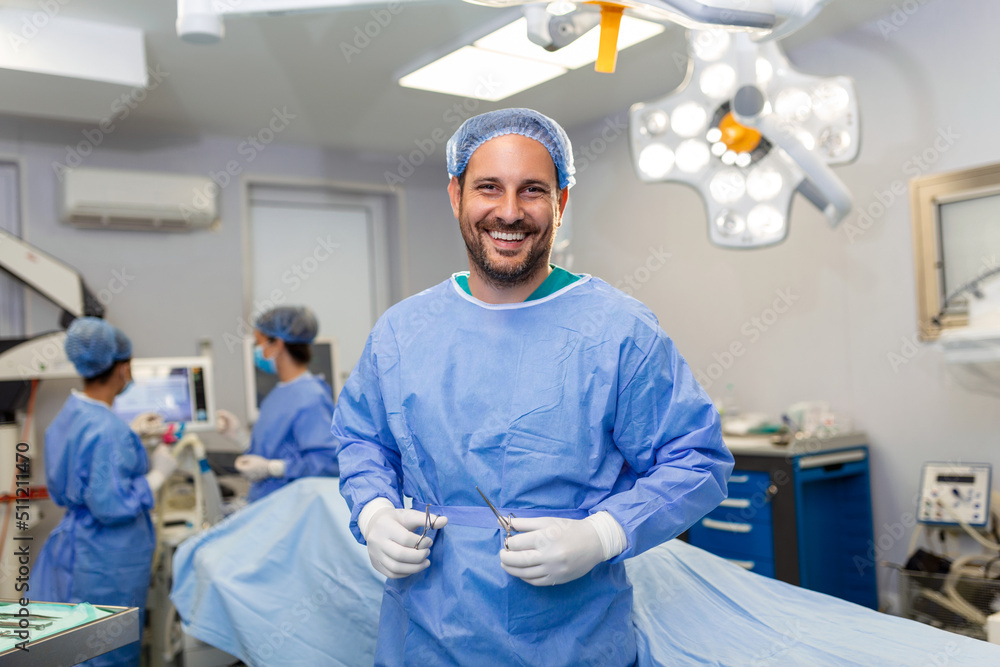 Portrait of male surgeon in operation theater looking at camera. Doctor in scrubs and medical mask in modern hospital operating theater.