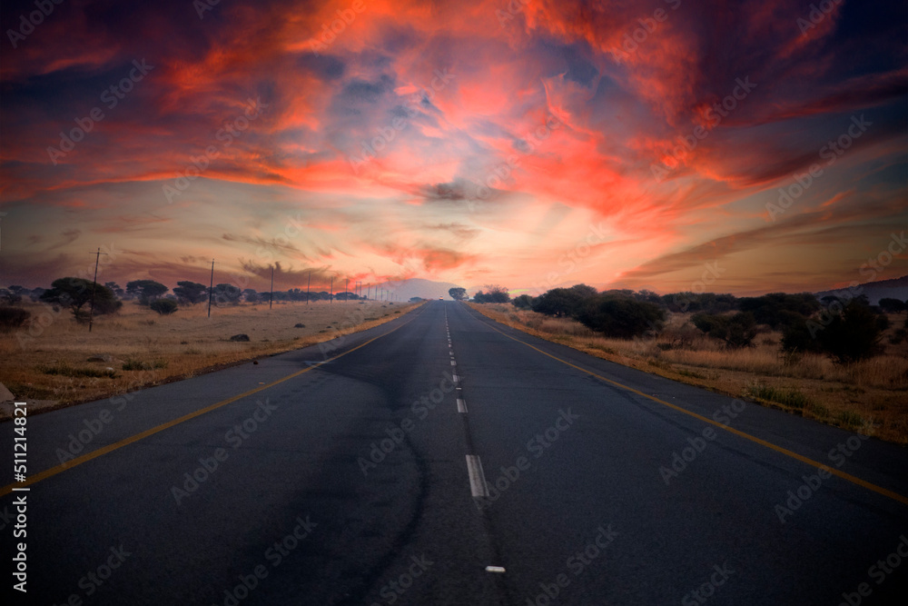 Naklejka premium Beautiful South African road that runs through the middle of the African savannah under the typical African sun, which is characterized by beautiful colors at sunset.