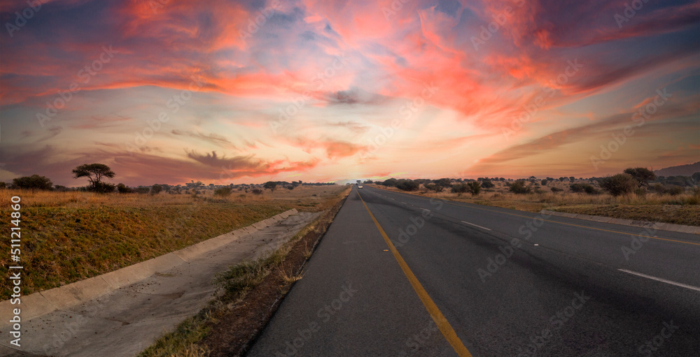 Travel on a road that runs through the middle of the African savannah of South Africa at sunset, it is a beautiful road with a beautiful sky with typical colors of the African sun.