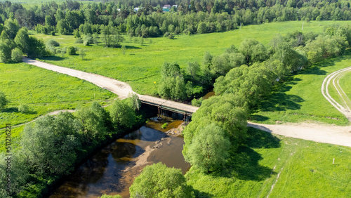 A bird's-eye view of the road and a small bridge over a small flat river. The concept of a tourist holiday, a simple bridge over a small river. Summer landscape, river with a car bridge