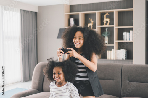 Happy two young girl playing video game during sitting on sofa at home together