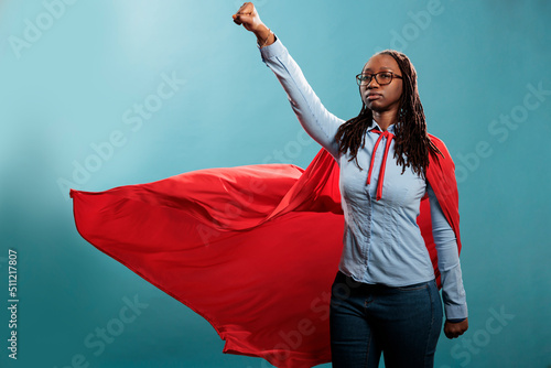 Fototapeta Powerful and brave young superhero woman wearing hero costume while posing as flying on blue background