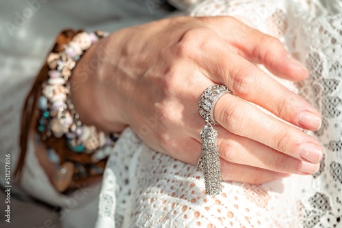 Close up of beautiful tribal boho style woman hands with lots of accessories. Boho style for fashionable look on resort. Middle aged well looking woman in white dress and boho style braclets.