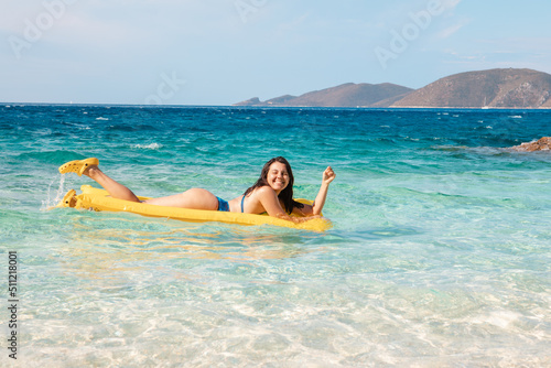 happy woman in blue swimsuit floating on yellow inflatable mattress