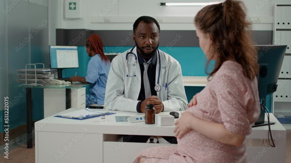 Male obstetrician having checkup appointment with pregnant patient, talking about maternity and childbirth in medical cabinet. Health specialist consulting woman with pregnancy belly. Male obstetrician having checkup appointment with pregnant patient, talking about maternity and childbirth in medical cabinet. Health specialist consulting woman with pregnancy belly.