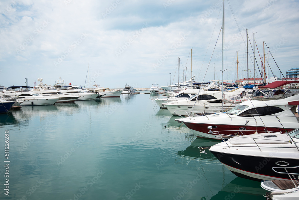 Luxury yachts docked in sea port. Marine parking of modern motor boats and azure water. Tranquility, relaxation and fashionable vacation. White yachts and sailboats moored in marina, summer season.
