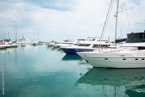 Luxury yachts docked in sea port. Marine parking of modern motor boats and azure water. Tranquility, relaxation and fashionable vacation. White yachts and sailboats moored in marina, summer season.