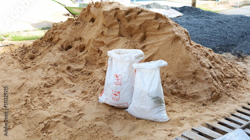 White sandbags and piles of sand. Close-up of old plastic sacks reused to contain sand for construction in outdoor construction sites. Selective focus