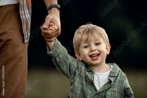фотографія dad holds the hand of a happy kid, a little boy smiles