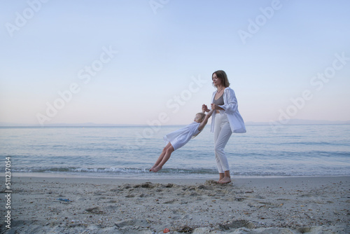 Mother and daughter having fun on the beach. Mother holding girls hands and spinning around. Family outdoor activities concept.	