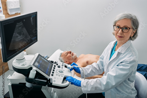 Sonographer occupation. Portrait of sonographer near the ultrasound machine at medical clinic during male patient's body ultrasound scan photo