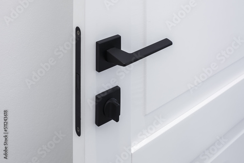 Modern black door handle on white wooden door in interior. Knob close-up elements. Door handle, fittings for interior design photo