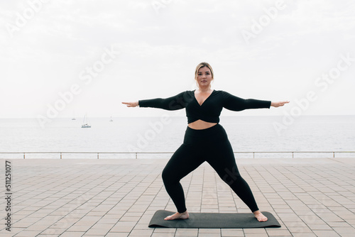 plus size girl practicing yoga in front of the ocean