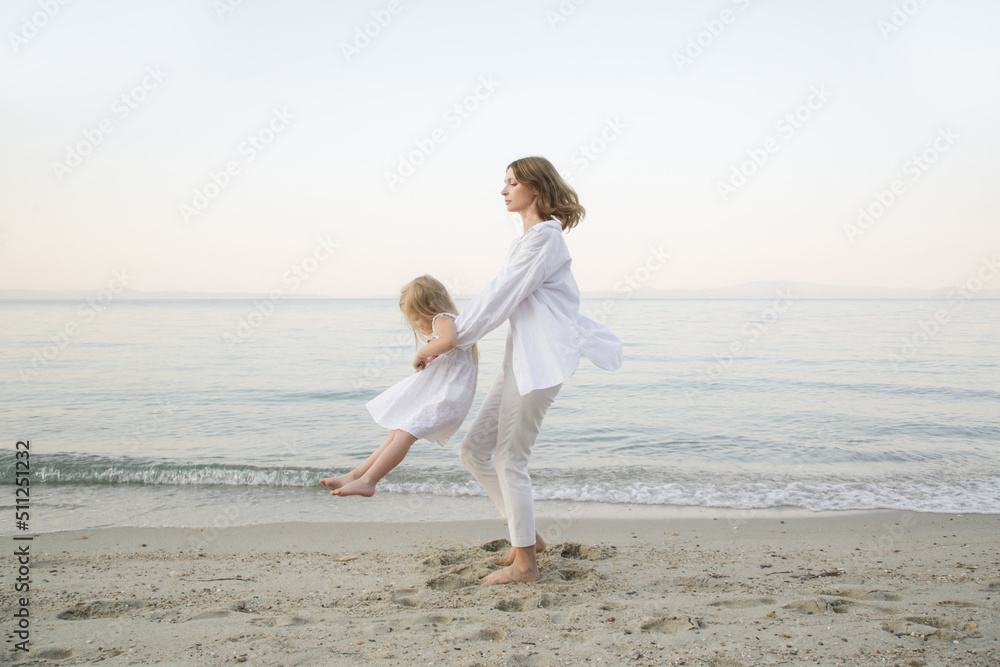 Mother and daughter having fun on the beach. Mother holding girls hands and spinning around. Family outdoor activities concept.	