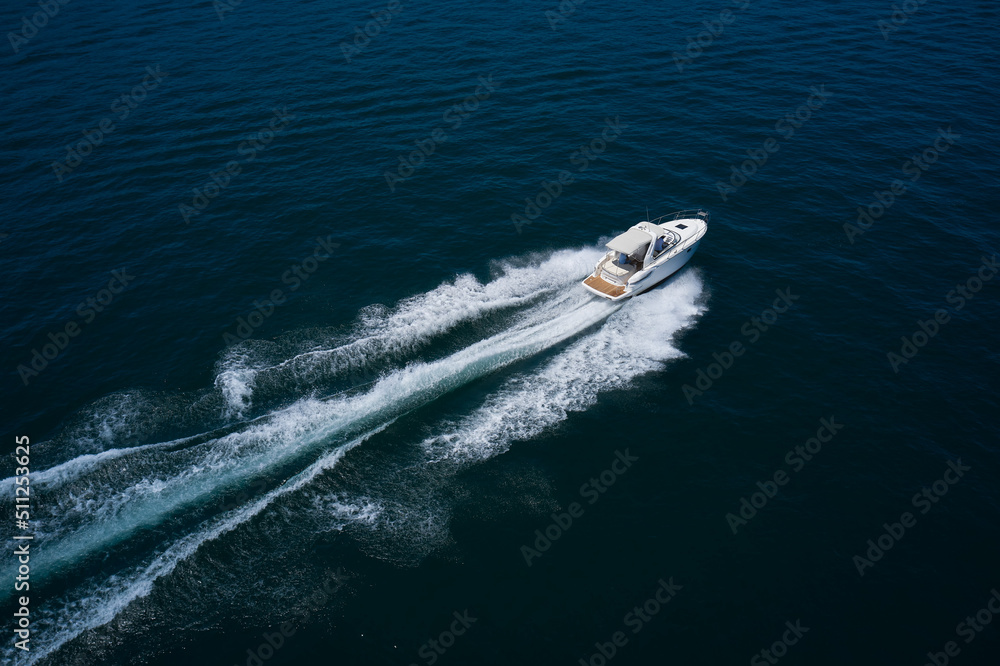 White yacht fast moving on clear water aerial side view. A large white boat at high speed on the water leaves a white trail, top view White yacht fast moving on clear water aerial side view. A large white boat at high speed on the water leaves a white trail, top view