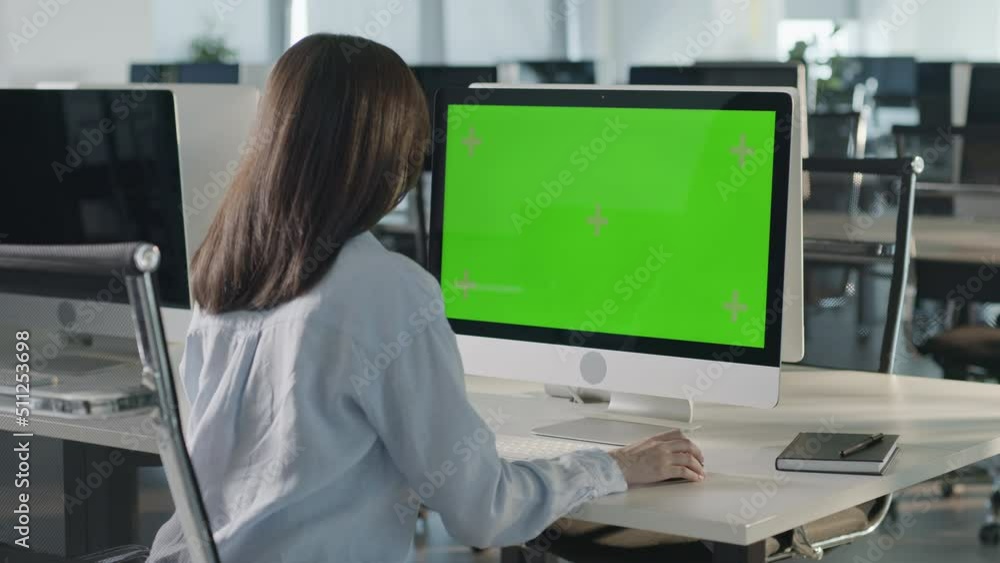 Creative Young Woman Sitting at His Desk Using Desktop Computer with Mock-up Green Screen. Evening in the Stylish Office Studio. Beautiful Diverse Female Manager Surfing Internet in Green Screen Creative Young Woman Sitting at His Desk Using Desktop Computer with Mock-up Green Screen. Evening in the Stylish Office Studio. Beautiful Diverse Female Manager Surfing Internet in Green Screen