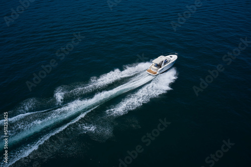 White yacht fast moving on clear water aerial side view. A large white boat at high speed on the water leaves a white trail, top view