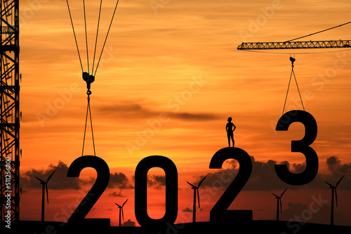 Concept Happy new year 2023 Silhouette of engineer and construction to create lifting crane 2023 on sunset background.