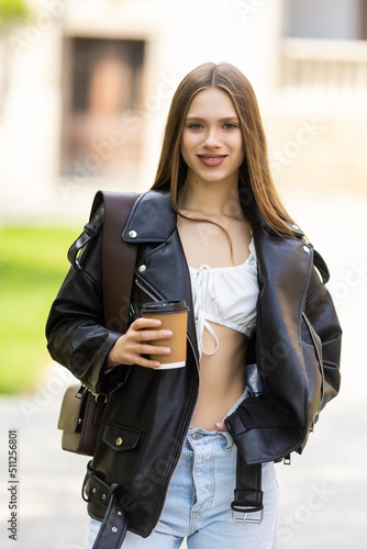 Young woman walking in the city street and drinking take away coffee in paper cup.