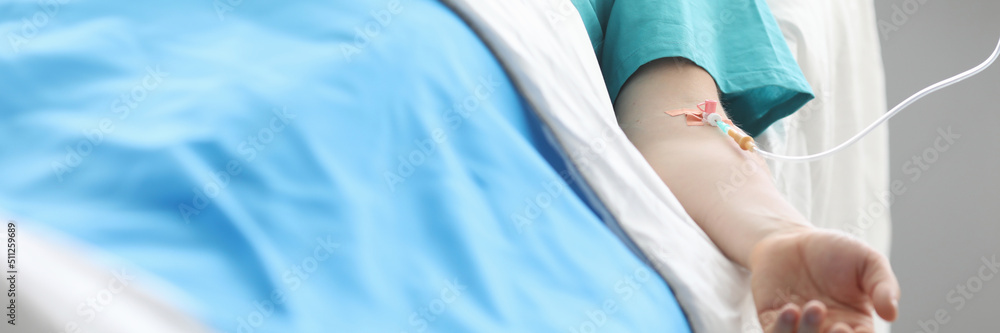 Fototapeta premium Male patient lying on bed with intravenous drip in his hand closeup
