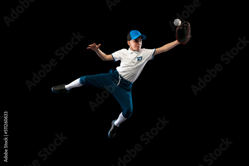 Photography Dynamic portrait of little baseball player, pitcher in blue-white uniform training isolated on black studio background