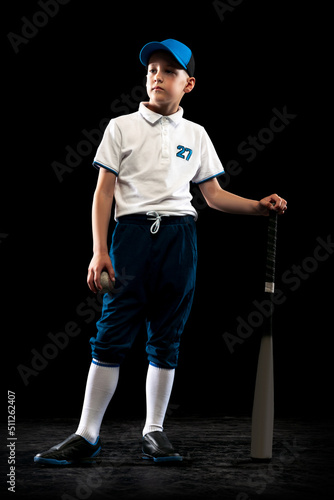 Full-length portrait of kid, beginner baseball player in sports uniform posing with baseball bat isolated on dark background. Concept of sport, achievements, competition