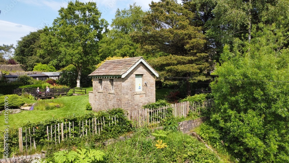 Old stone building in the grounds of Whalley abbey surrounded by large trees and gardens. 
