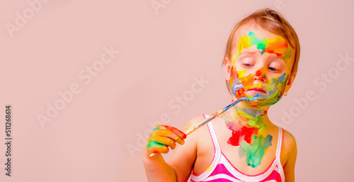 Little cute girl making herself children's makeup with brush and colorful painted hands. Beauty, leisure, happy childhood and art concept. Copy space.