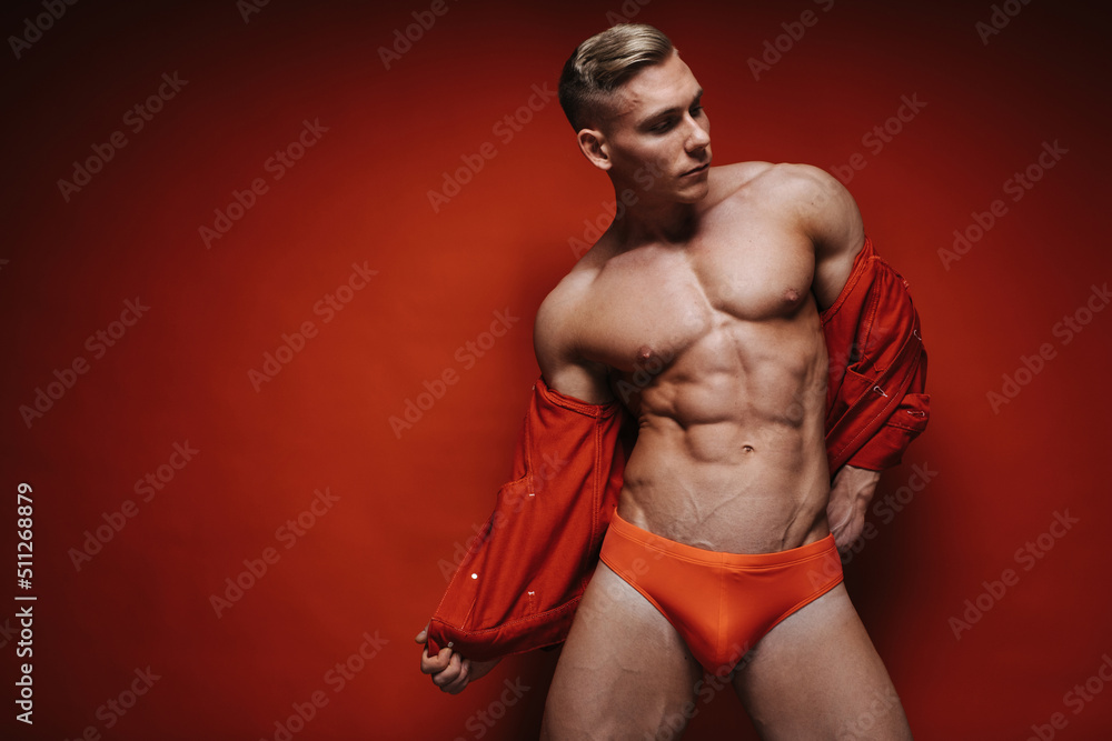 En el nombre capital Enseñando Fotografia do Stock: Sexy young man in red speedo and jean jacket stripping  at red background. Handsome shirtless guy taking off his red jacket.  Fitness male model in studio. Muscular sportsman with