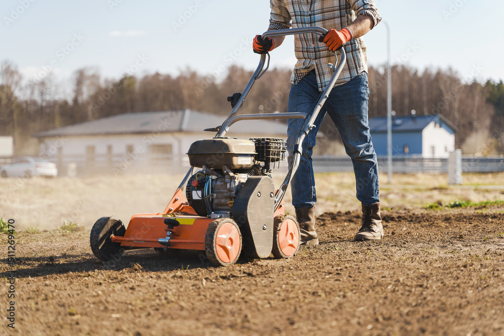 Obraz premium Man using aerator machine to scarification and aeration of lawn or meadow