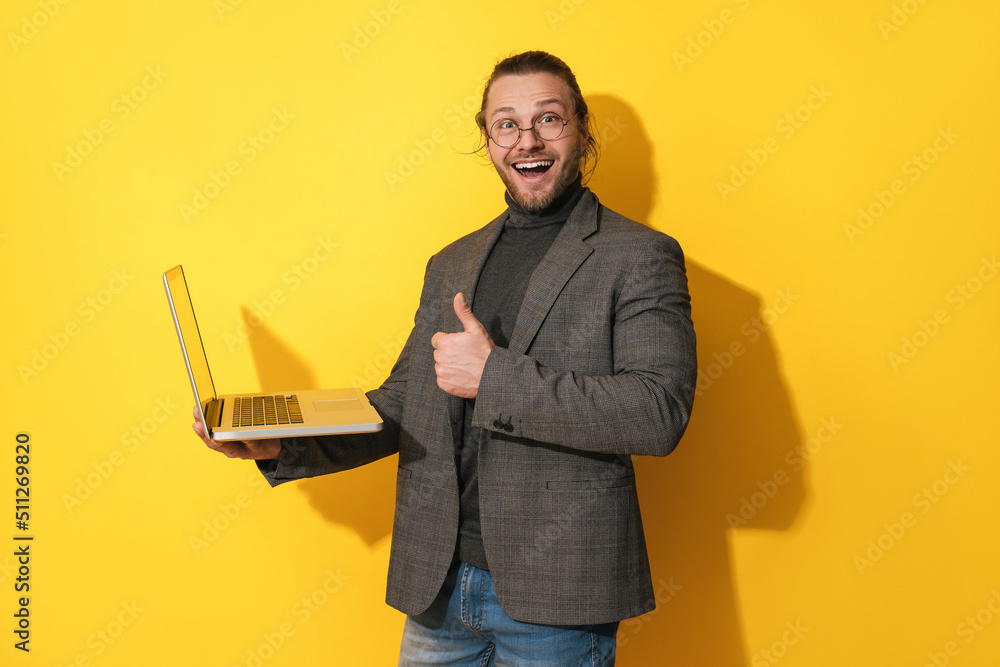 Happy bearded man wearing eyeglasses is using laptop and giving the common thumb sign of approval