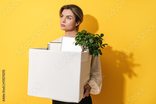 Woman holding box with personal items after job resignation against yellow background