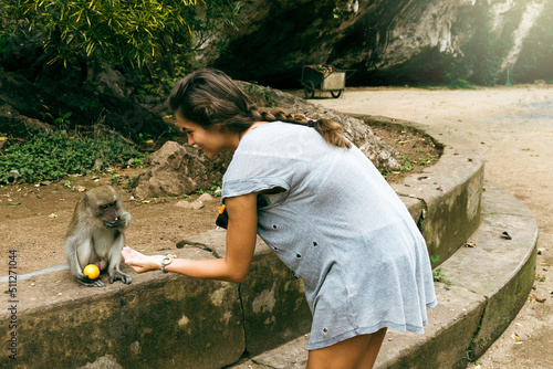 Wall Mural Young female tourist feeding monkey with fruits in Thailand.