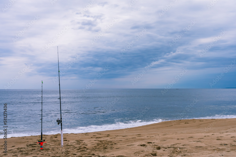 Two fishing rods standing on stands on a sandy beach in Florida in cloudy weather