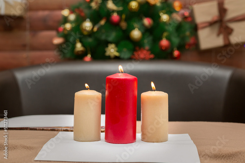 Three large burning candles on the background of a decorated Christmas tree with toys, a symbol of the new year.