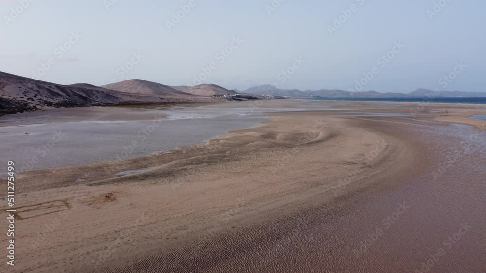 Aerial view of Playa de Jandia in Fuerteventura - the waves of the sea invade the sand - the sea towers above the beach and a woman walks alone Aerial view of Playa de Jandia in Fuerteventura - the waves of the sea invade the sand - the sea towers above the beach and a woman walks alone