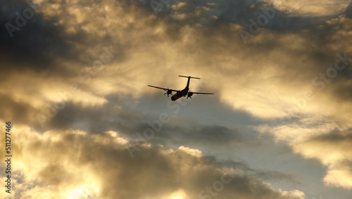 Silhouette of an airplane flying at sunset clouds.