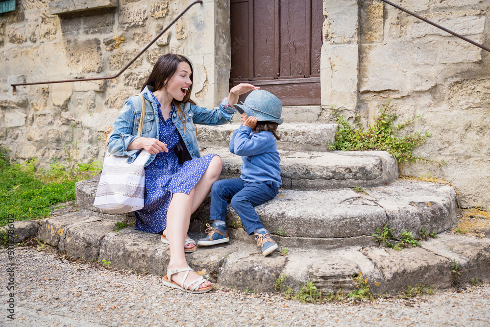 Mother and little handsome baby boy sitting on ancient stone stairs and playing outdoor with straw hat in old town Mother and little handsome baby boy sitting on ancient stone stairs and playing outdoor with straw hat in old town