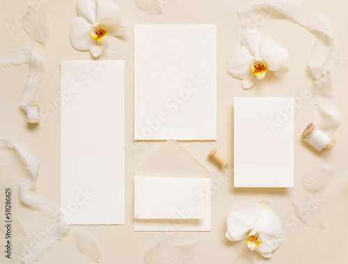 Wedding cards near white orchid flowers and silk ribbons on light yellow, suite mockup