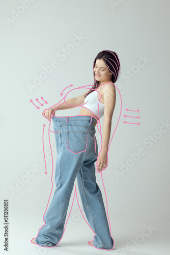 Photography Portrait of slim woman in underwear wear posing in giant oversized jeans isolated over gray studio background