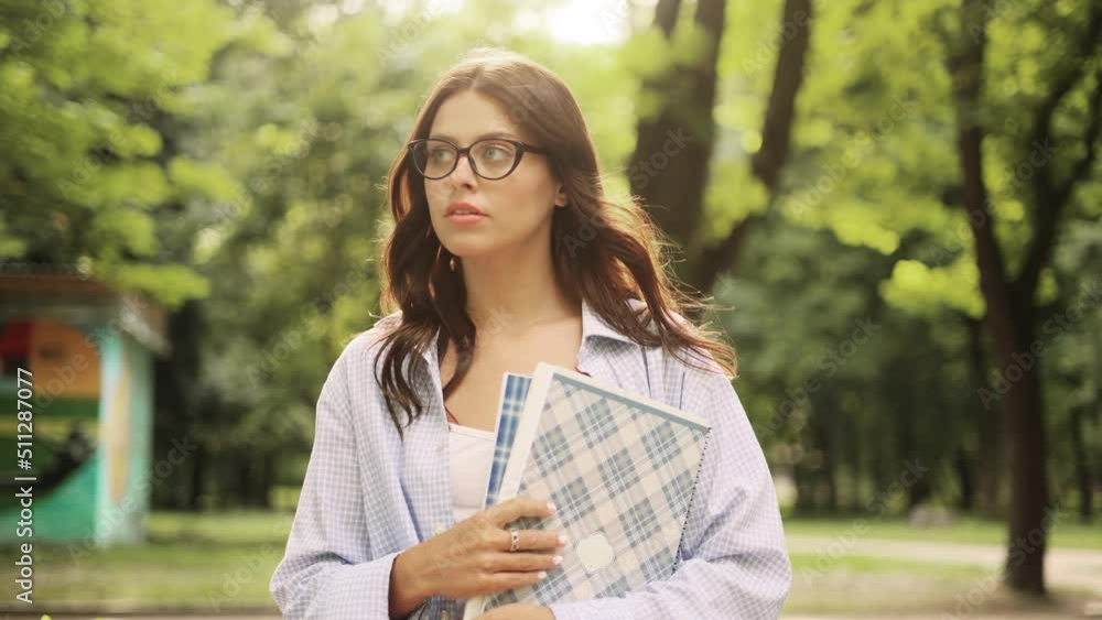Portrait of student girl with eyeglasses standing with books near the park and looking at the camera. Portrait of attractive brunette girl. Portrait of student girl with eyeglasses standing with books near the park and looking at the camera. Portrait of attractive brunette girl.