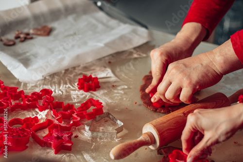 Close-up photo of hands. Man and woman cut out dough cookies. Christmas pastries, cozy kitchen, unrecognizable people. Red color. New year Eve.