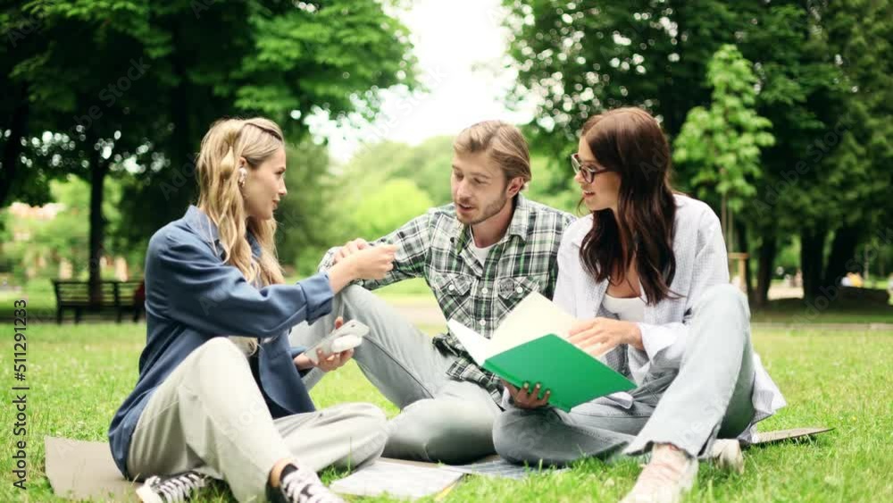 Group of college students study outside together. Portrait of  young friends preparing for exams at campus park.