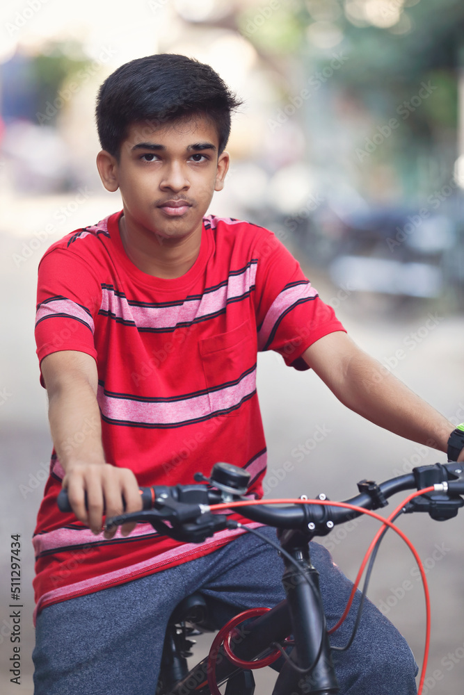 Obraz premium Indian teenage boy with backpack riding bicycle on city street 