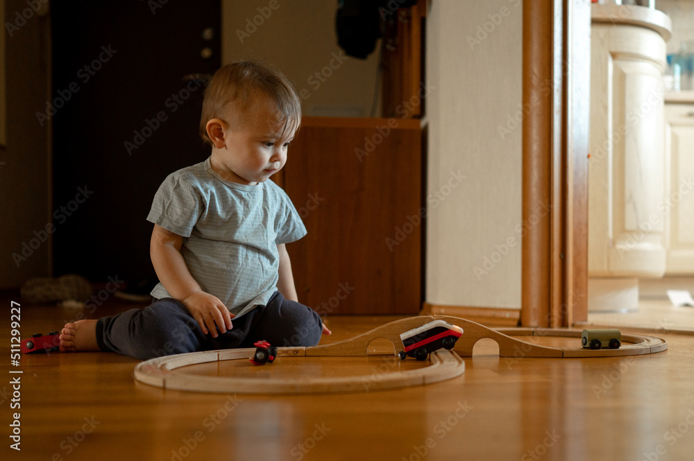 A child playing a toy railway train. The child is sitting on the floor with wooden toys. Toys for a little boy. A preschooler builds a railway and blocks at home, in kindergarten. Educational games fo A child playing a toy railway train. The child is sitting on the floor with wooden toys. Toys for a little boy. A preschooler builds a railway and blocks at home, in kindergarten. Educational games fo