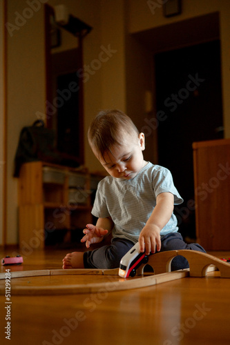 A child playing a toy railway train. The child is sitting on the floor with wooden toys. Toys for a little boy. A preschooler builds a railway and blocks at home, in kindergarten. Educational games fo